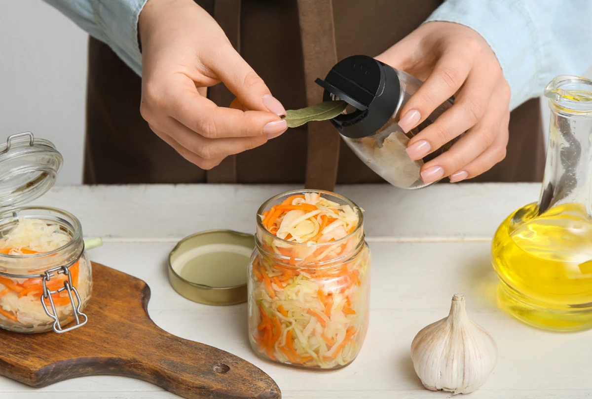 Kobieta dodaje liść laurowy do sałatki z kapusty i marchewki w słoiku
