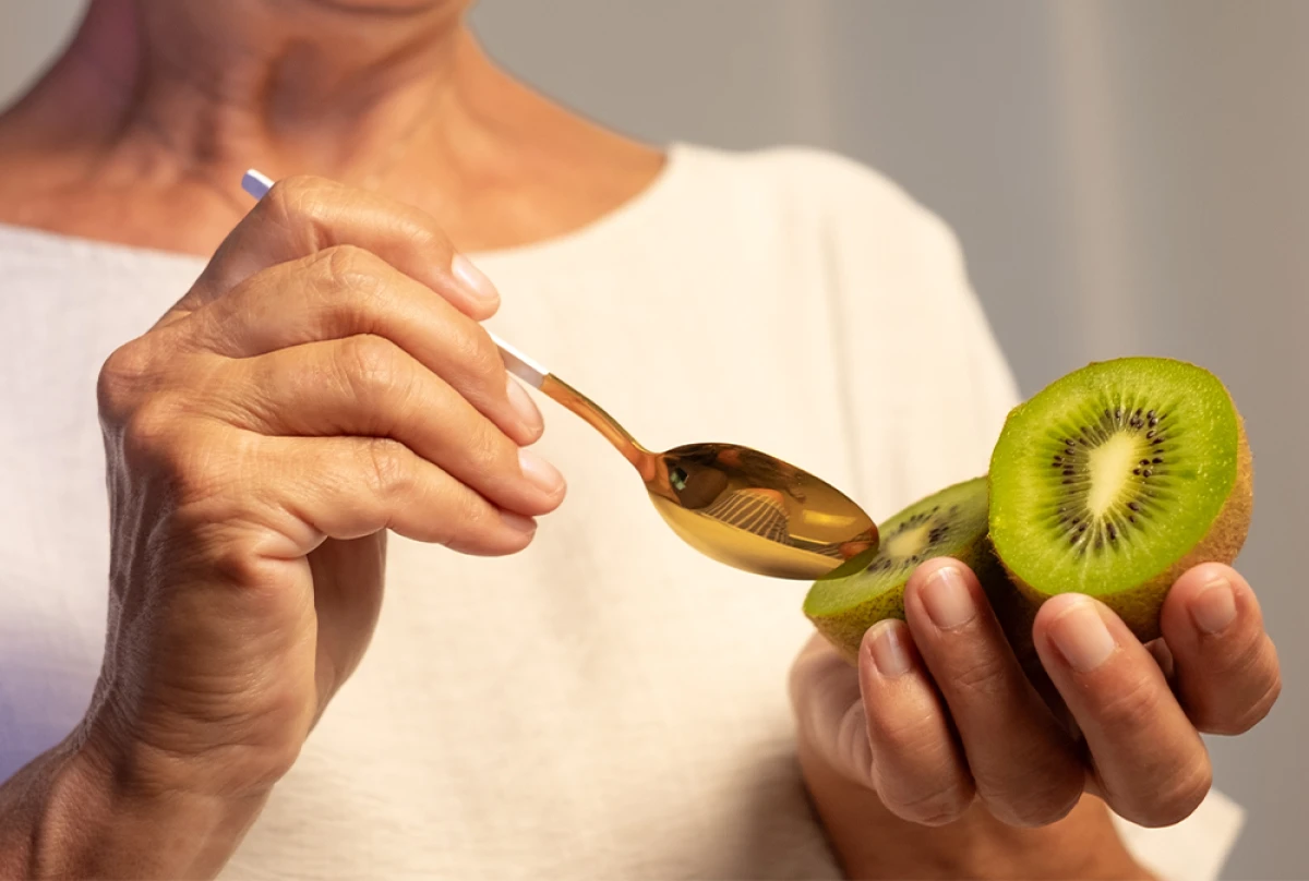 Kobieta je łyżeczką przekrojone na pół kiwi