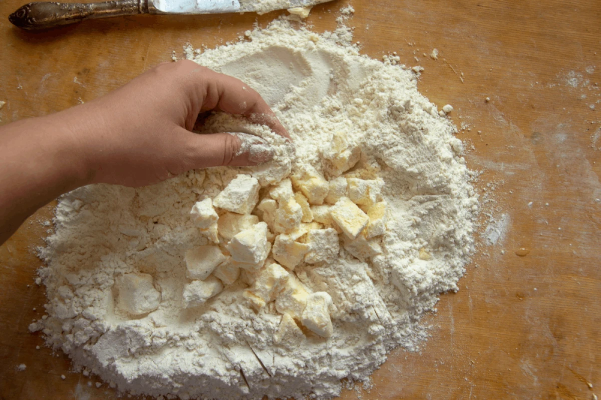 Kobieta rozciera zimne masło z mąką końcami palców