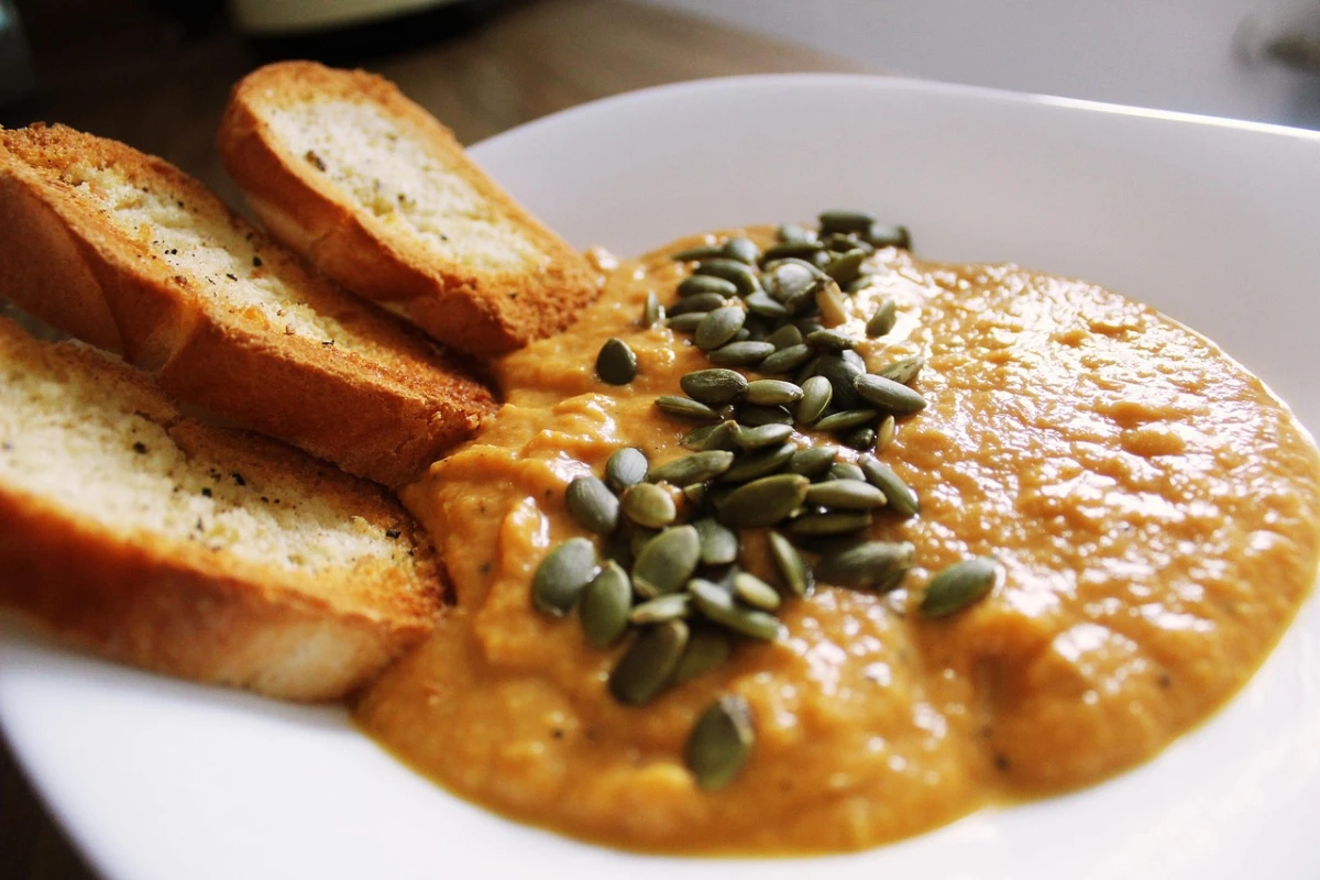 Kremowa zupa dyniowa podana w białej misce, posypana pestkami dyni, z grzankami z bagietki ułożonymi z boku