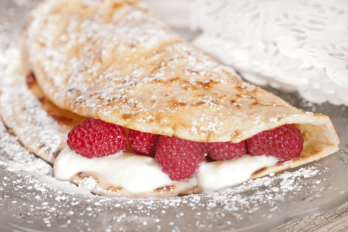 Naleśnik z sosem waniliowym i malinami posypany cukrem pudrem