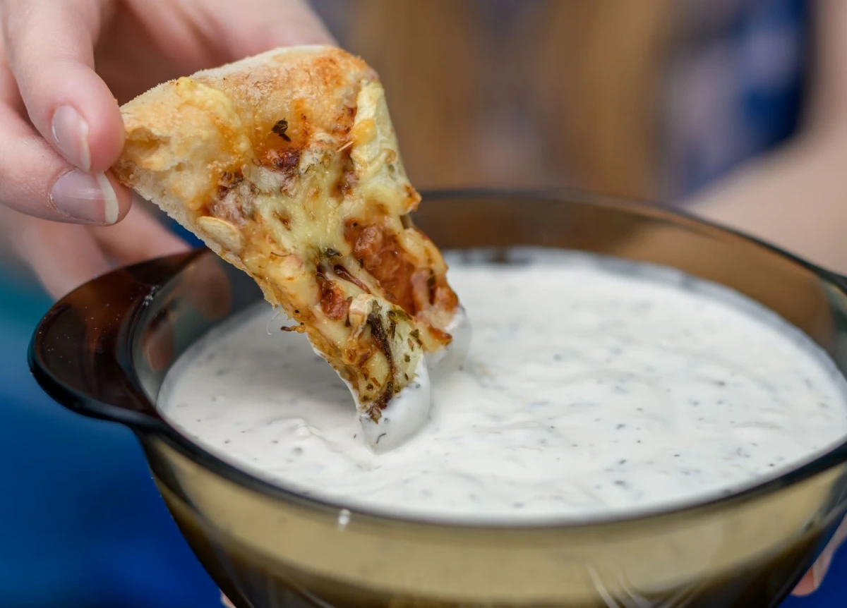 Osoba macza kawałek pizzy w sosie czosnkowym