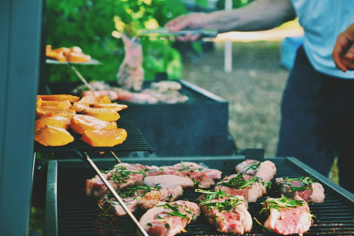 Osoba stoi przy grillu, na którym leżą kawałki mięsa i brzoskwiń.