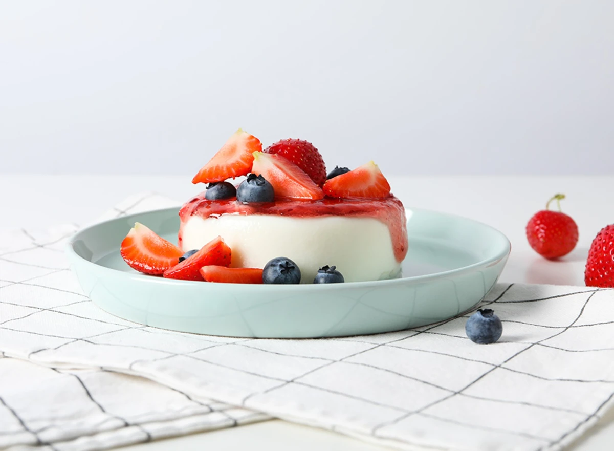 Panna cotta podana z truskawkami i borówkami na niebieskim talerzu