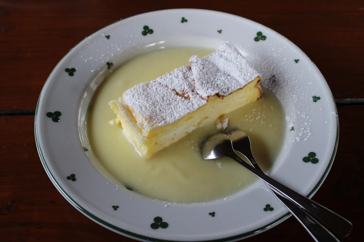 Porcja domowego ciasta podana w głębokim talerzu z sosem waniliowym i posypana cukrem pudrem