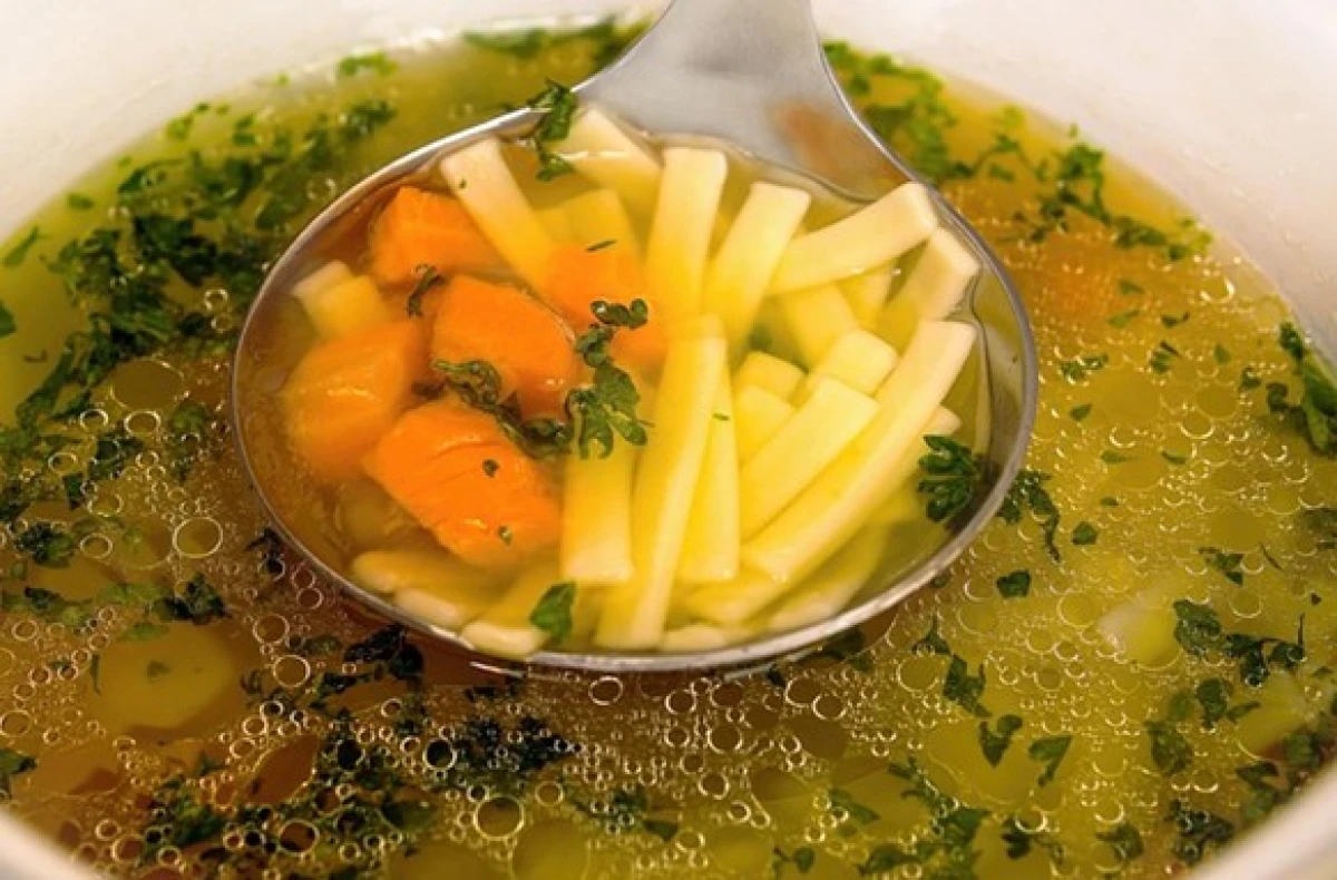 Chochla zanużona w wazie z esencjonalnym rosołem z makaronem i marchewką