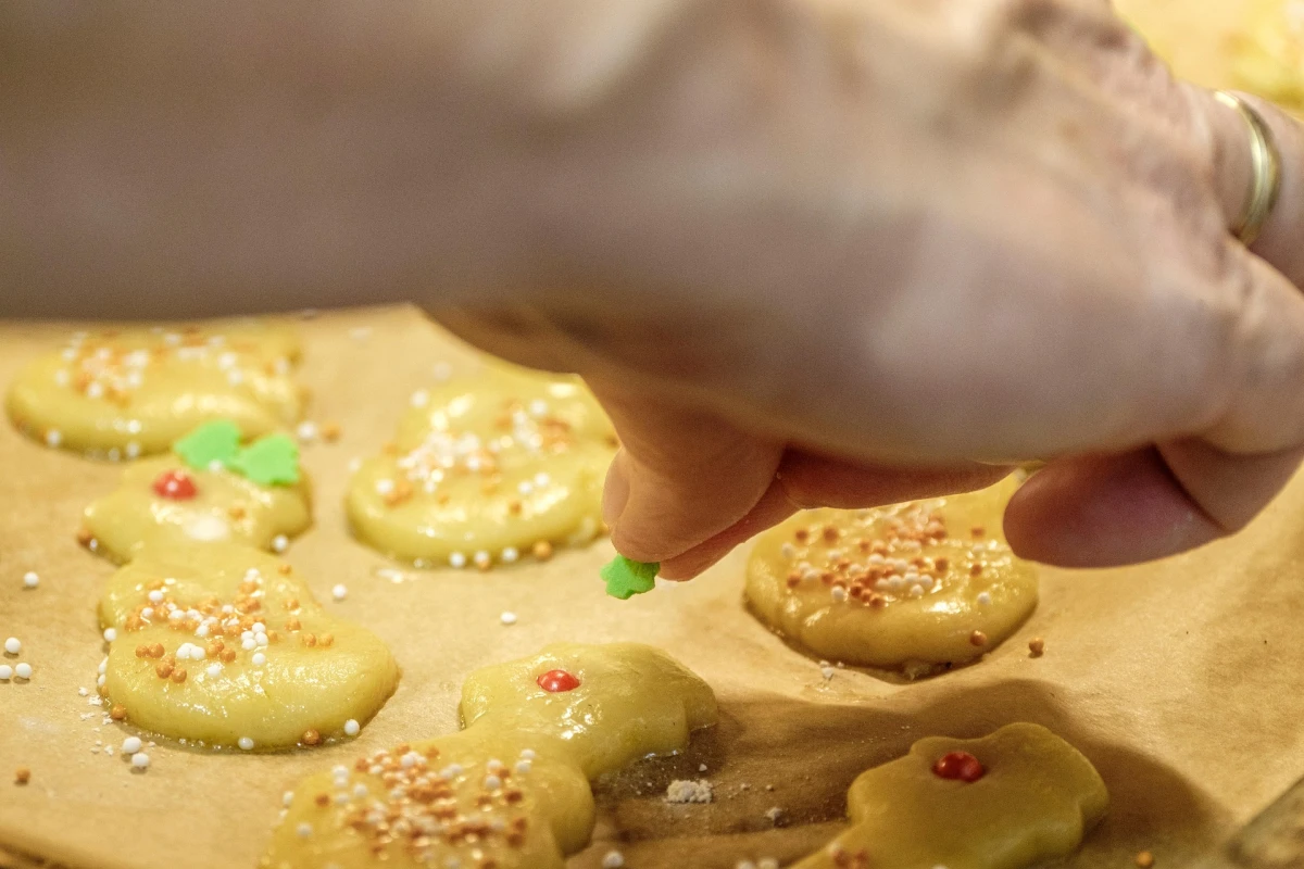 Na blasze wyłożonej papierem do pieczenia znajdują się surowe ciastka obsypane kolorową posypką