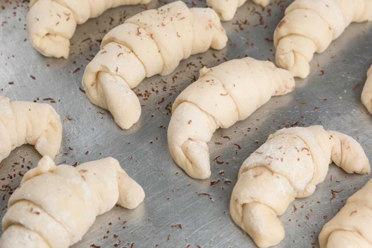 Surowe rogaliki ułożone na blacie - przygotowane i sformowane przed pieczeniem
