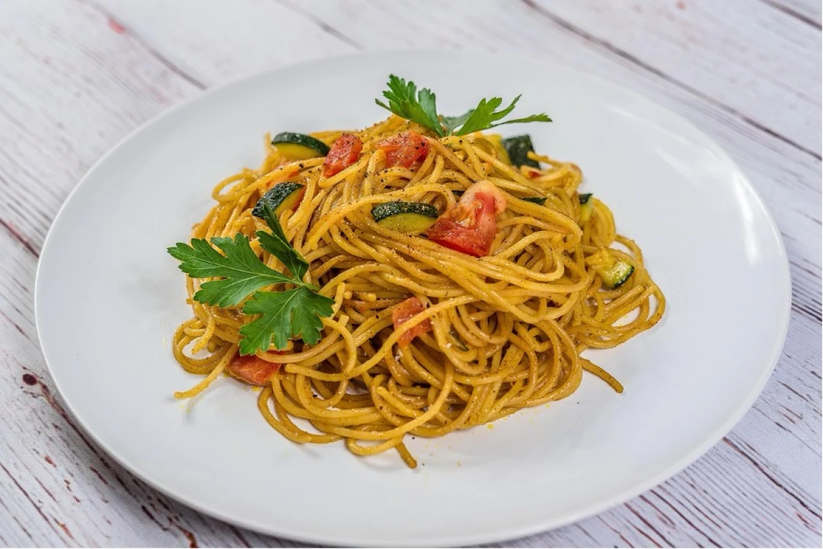 Ugotowany makaron spaghetti z pomidorami, cukinią i pietruszką na białym talerzu