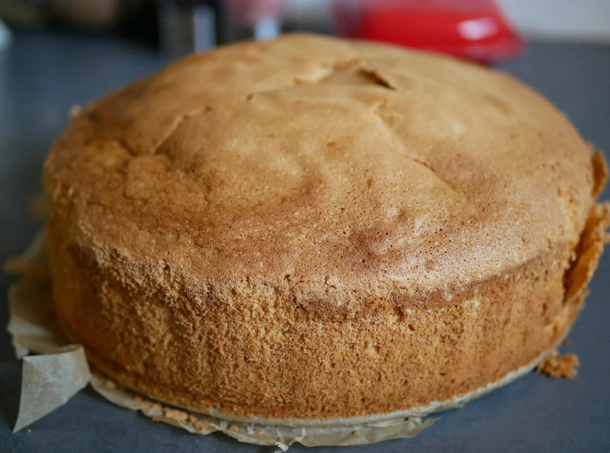 Upieczony, złocisty biszkopt bez dekoracji, leżący na papierze do pieczenia na kuchennym blacie