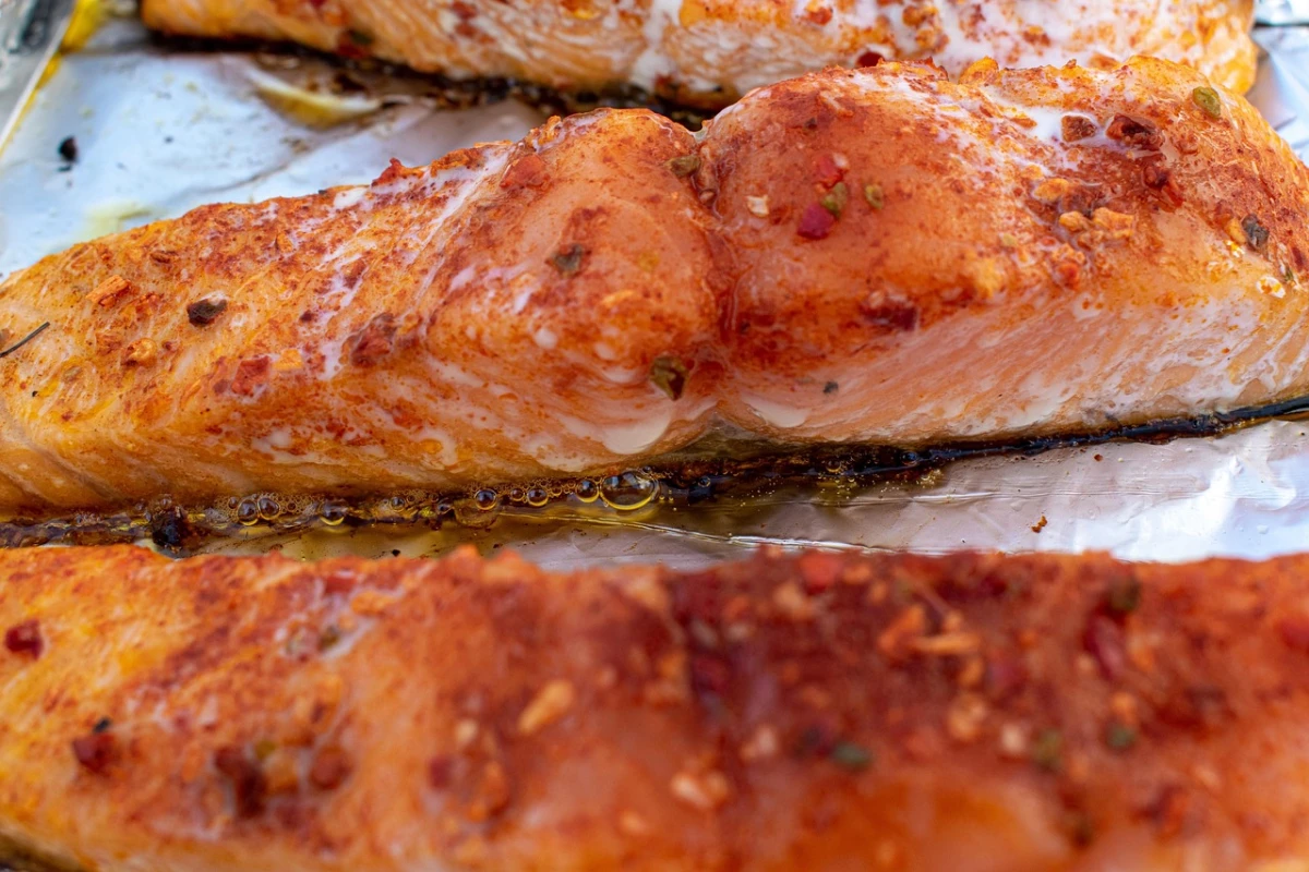 Zbliżenie na pieczone łososie w przyprawach, leżące na folii aluminiowej, z widocznym apetycznym sosem