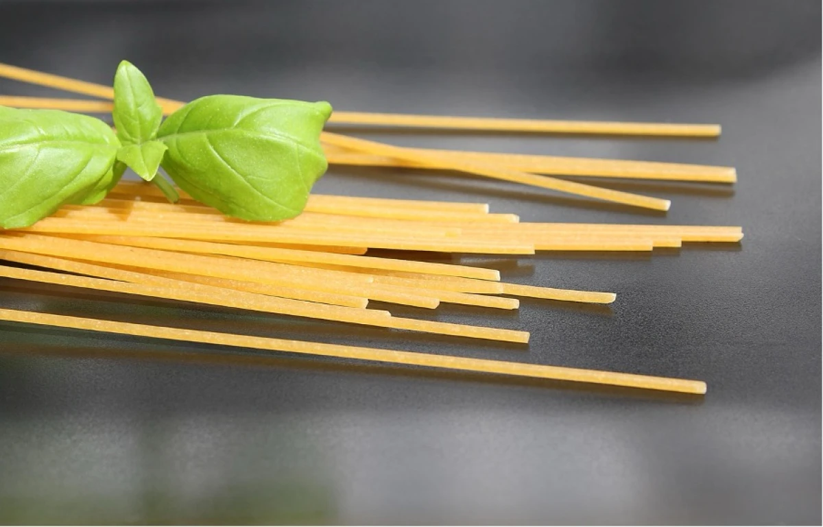 Zbliżenie na surowy makaron spaghetti z listkiem bazylii