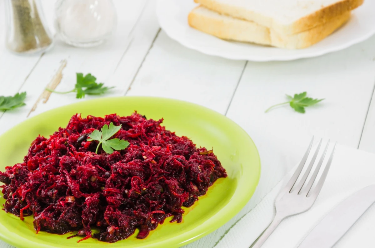 Buraczki zasmażane leżą na talerzu w kolorze limonowym, obok leży widelec