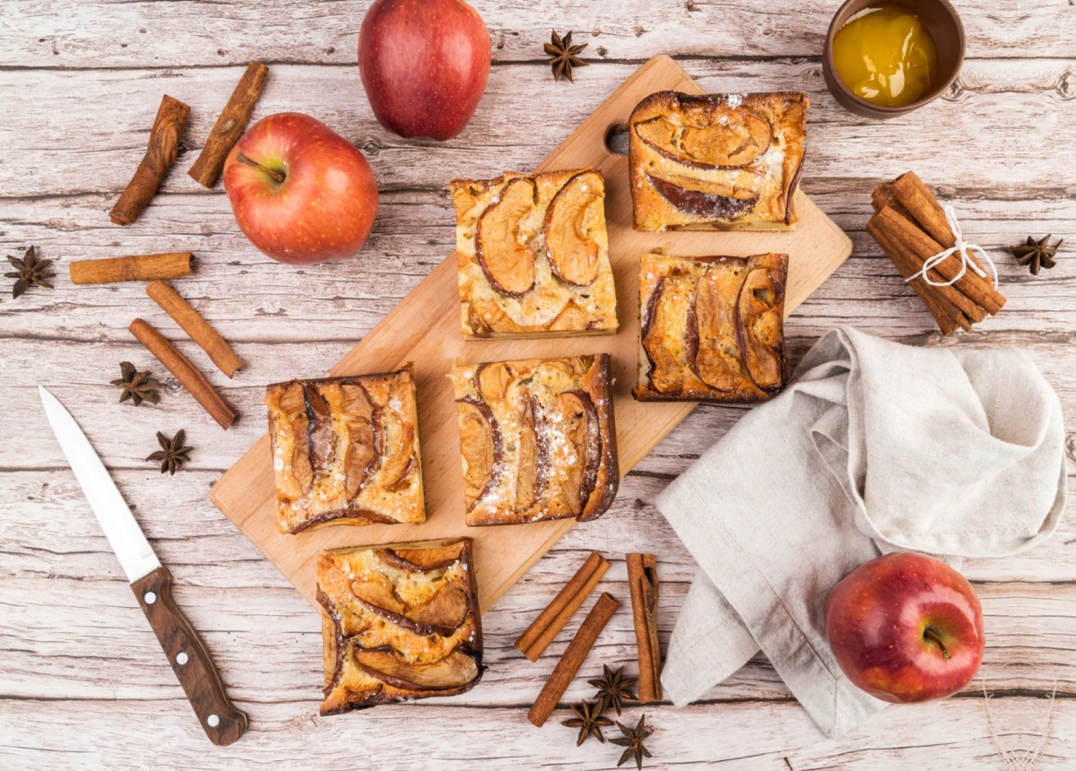 Upieczone ciastka francuskie z jabłkami leżą na drewnianej deszcze, obok leżą jabłka i laski cynamonu