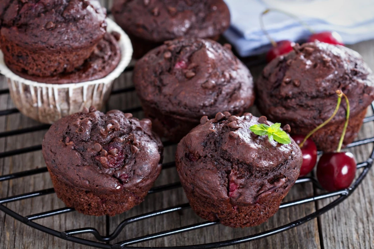 Czekoladowe muffinki z wiśniami leżą na czarnej kratce