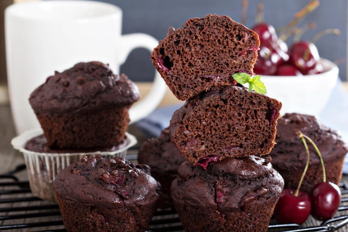 Czekoladowe muffinki z wiśniami leżą na czarnej kratce