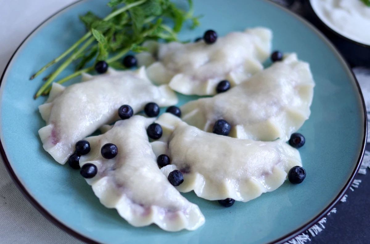 Pierogi z jagodami i białą czekoladą na niebieskim talerzu