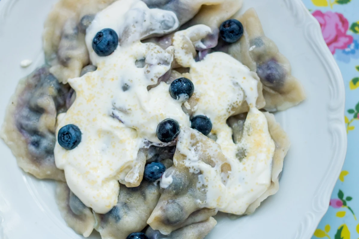 Pierogi z jagodami i białą czekoladą polane śmietaną