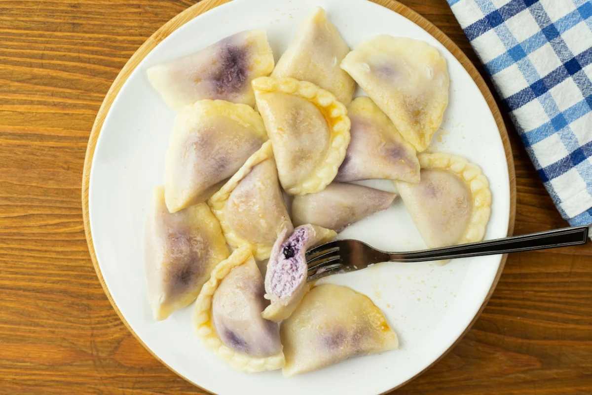 Talerz ugotowanych pierogów z jagodami, pół pieroga nabite na widelec
